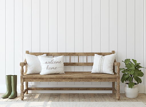 Image of a bench with a welcome home pillow against white vertical paneling.