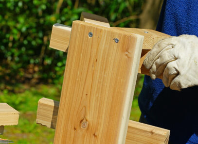 How To Build a DIY Picnic Table - Timber Mart - close up of a gloved hand holding a wooden section of a picnic table.