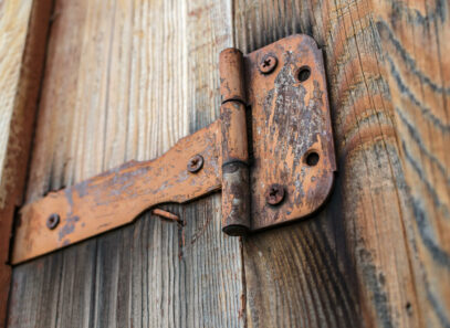 Outdoor Hardware - Timber Mart - close up of a rusty door hinge on a weathered wooden gate.