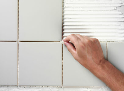 A hand places a tile spacer between white ceramic tiles on a kitchen backsplash