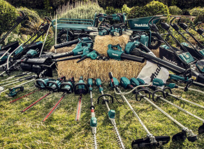The full lineup of Makita landscaping tools laid out on a hay bale and lawn.